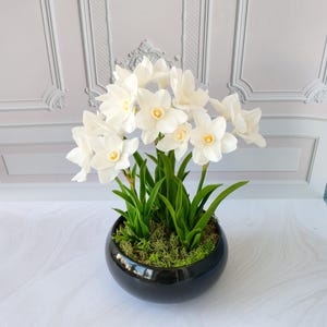 Puede incluir: Una taza de cerámica blanca con un asa negra y el texto "But First, Coffee" en negro, con una fuente de estilo manuscrito. La taza está sobre una superficie blanca.