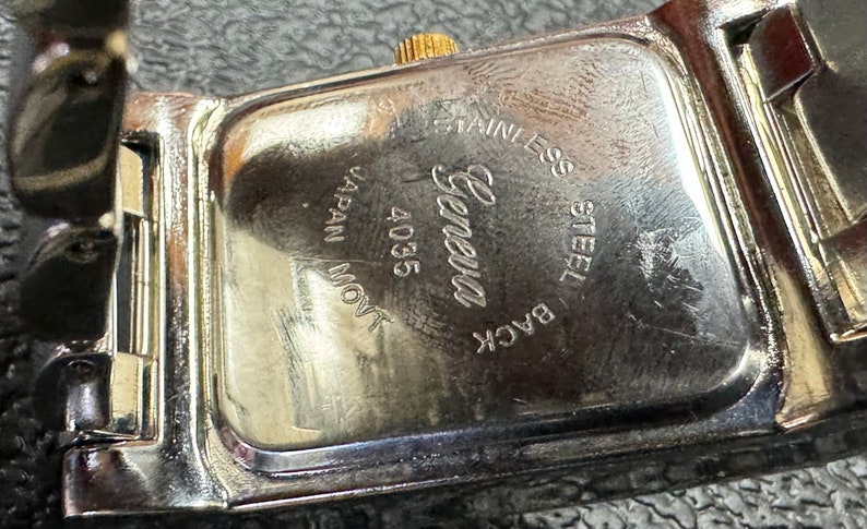 K&ouml;nnte beinhalten: Nahaufnahme der R&uuml;ckseite einer silbernen Uhr mit der Gravur "Back Steel Stainless Geneva 4035 Japan Movt".