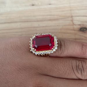 May include: A gold ring with a large, red, rectangular gemstone surrounded by smaller, clear gemstones.