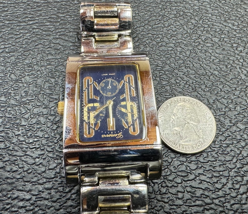 K&ouml;nnte beinhalten: Eine Herren-Armbanduhr in Silber und Gold mit schwarzem Zifferblatt und drei Chronographen-Zifferbl&auml;ttern. Die Uhr hat ein Edelstahlband und ein rechteckiges Geh&auml;use.