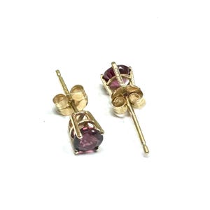 May include: A pair of gold stud earrings with round, dark purple gemstones.