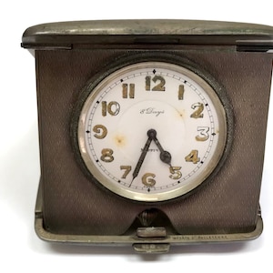 May include: A silver-toned, 8-day, mechanical, pocket watch with a white face and black hands. The watch is in a silver-toned case with a hinged lid. The case has a textured surface and the words "Imported of Angleterre" are engraved on the bottom.