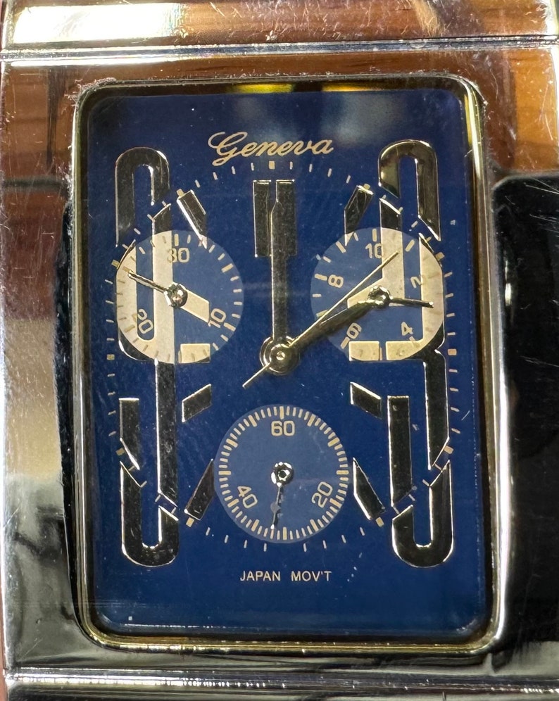 K&ouml;nnte beinhalten: Eine silberne und goldene Chronographen-Armbanduhr mit blauem Zifferblatt. Das Zifferblatt der Uhr hat drei Hilfszifferbl&auml;tter und den Text "Geneva" und "JAPAN MOV'T".