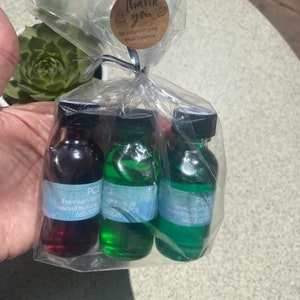 K&ouml;nnte beinhalten: Drei kleine Glasflaschen gef&uuml;llt mit roter, hellgr&uuml;ner und dunkelgr&uuml;ner Fl&uuml;ssigkeit, jeweils mit schwarzem Verschluss und einem hellblauen Etikett mit dem Text PCE Premium fragrance oil. Die Flaschen sind in einem durchsichtigen Plastikbeutel verpackt, der mit einem runden braunen Aufkleber mit der Aufschrift thank you for supporting my small business versehen ist.