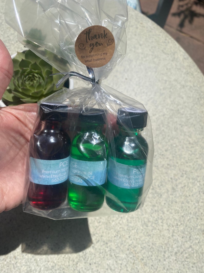 K&ouml;nnte beinhalten: Drei kleine Glasflaschen gef&uuml;llt mit roter, hellgr&uuml;ner und dunkelgr&uuml;ner Fl&uuml;ssigkeit, jeweils mit schwarzem Verschluss und einem hellblauen Etikett mit dem Text PCE Premium fragrance oil. Die Flaschen sind in einem durchsichtigen Plastikbeutel verpackt, der mit einem runden braunen Aufkleber mit der Aufschrift thank you for supporting my small business versehen ist.