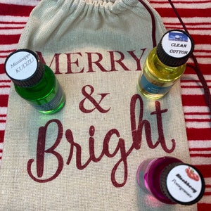 May include: A burlap bag with the words "Merry & Bright" printed on it. Three small glass bottles with labels are inside the bag. The labels read "Mississippi Kudzu", "Clean Cotton", and "Blackberry Fragrance".
