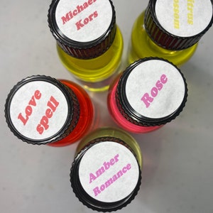 K&ouml;nnte beinhalten: F&uuml;nf kleine Glasflaschen mit schwarzen gerippten Verschl&uuml;ssen, von oben betrachtet. Die wei&szlig;en Etiketten auf den Verschl&uuml;ssen tragen den Text Michael Kors, Citrus blossom, Love spell, Rose und Amber Romance in verschiedenen Farben, mit gelber und roter Fl&uuml;ssigkeit.
