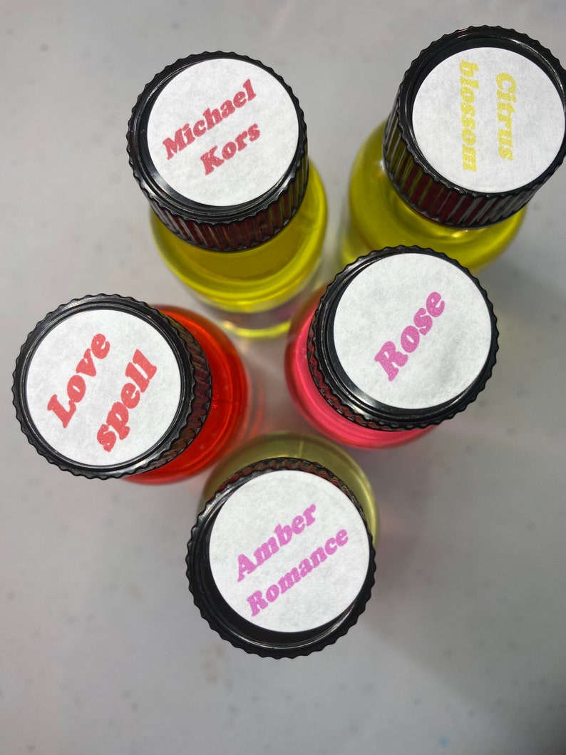 K&ouml;nnte beinhalten: F&uuml;nf kleine Glasflaschen mit schwarzen gerippten Verschl&uuml;ssen, von oben betrachtet. Die wei&szlig;en Etiketten auf den Verschl&uuml;ssen tragen den Text Michael Kors, Citrus blossom, Love spell, Rose und Amber Romance in verschiedenen Farben, mit gelber und roter Fl&uuml;ssigkeit.