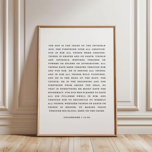 May include: A framed print with a light wood frame. The print features black text on a white background. The text is a passage from Colossians 1:15-20. The print is displayed on a white wall.