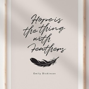 Op de afbeelding: Een ingelijste print met de quote "Hope is the thing with feathers" in elegant zwart schrift. Een zwarte veermotief staat onder de quote, met de naam van de auteur, Emily Dickinson, onderaan. De achtergrond is zacht beige.