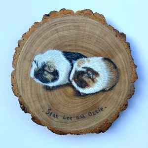 May include: A painted wooden slice with two guinea pigs, one black and white and one brown and white, with the text "Stan Lee and Ollie."