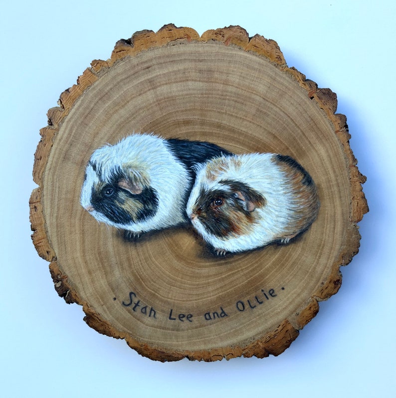 May include: A painted wooden slice with two guinea pigs, one black and white and one brown and white, with the text "Stan Lee and Ollie."