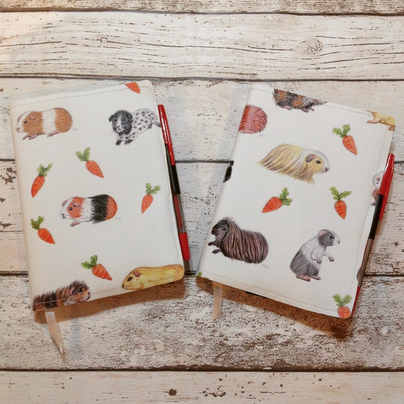 Peut inclure: Deux couvertures de livres blanches avec des motifs illustr&eacute;s d'animaux et de carottes. Les couvertures sont d&eacute;cor&eacute;es de cochons d'Inde, d'un lapin, d'un chien et d'un chat. Chaque couverture est associ&eacute;e &agrave; un stylo rouge.