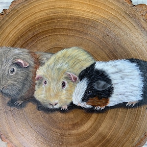 May include: A painting of three guinea pigs on a wooden slice. The guinea pigs are brown, white, and black and white. The painting is done in a realistic style.