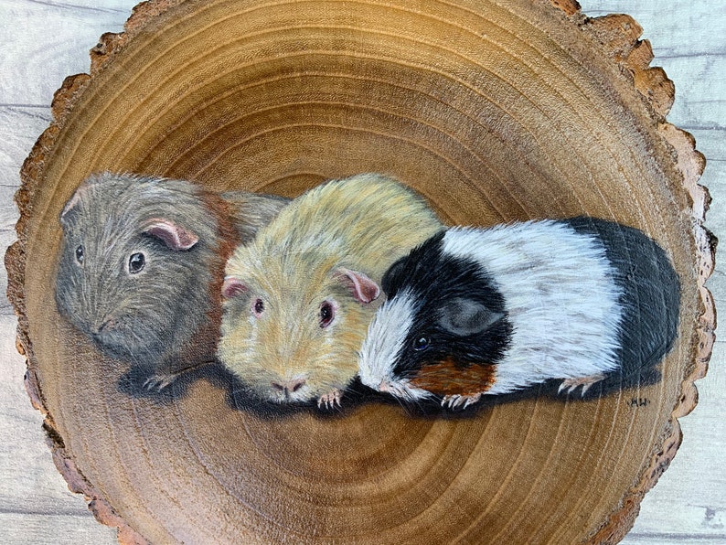 May include: A painting of three guinea pigs on a wooden slice. The guinea pigs are brown, white, and black and white. The painting is done in a realistic style.