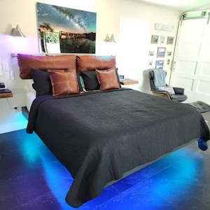 May include: A black bed with a black quilted bedspread and brown leather pillows. The bed is lit with blue LED lights underneath.