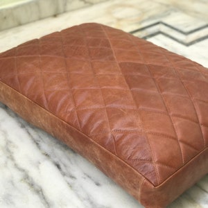 Pode incluir: Uma cama para cachorro de couro marrom com um padrão acolchoado de diamantes.