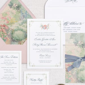 May include: A collection of wedding stationery, including invitations, RSVP cards, and envelopes. The invitations feature floral designs and elegant calligraphy. A light blue ribbon ties a card with a watercolor floral design. The stationery is arranged on a neutral surface.