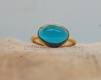 May include: A gold ring with a blue oval gemstone. The ring is set on a wooden surface.