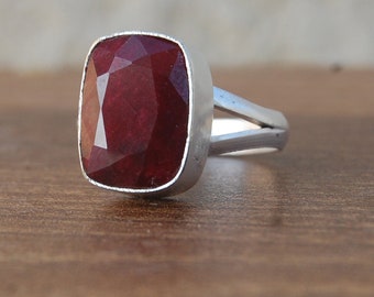 May include: A silver ring with a large, red, faceted gemstone. The ring has a simple, split band design.