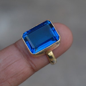 May include: A gold ring with a large, rectangular, blue gemstone.