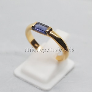 May include: A gold band ring with a single, rectangular, purple gemstone set in the center.