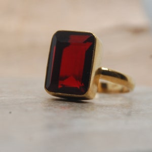 Puede incluir: Un anillo de oro con una gran piedra preciosa roja rectangular.