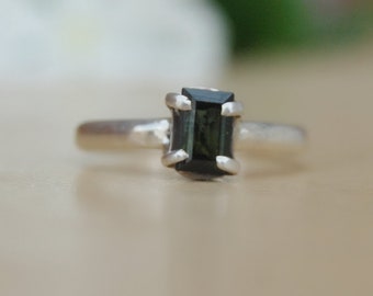 May include: A silver ring with a dark green emerald-cut gemstone.