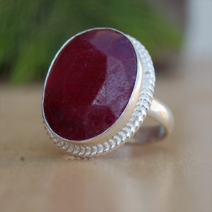 May include: A silver ring with a large, oval-shaped, dark red gemstone. The ring has a braided band.