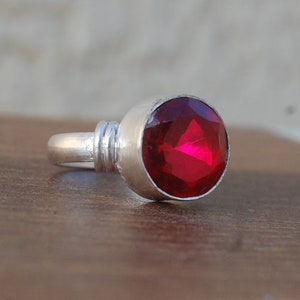 May include: A silver ring with a large, round, red gemstone.