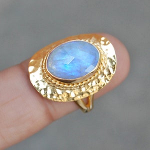 May include: A gold ring featuring a large oval moonstone set in a textured gold setting.
