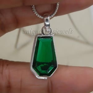 May include: A silver pendant necklace with a large, faceted, emerald green gemstone. The pendant is shaped like a teardrop and has a simple, elegant design.