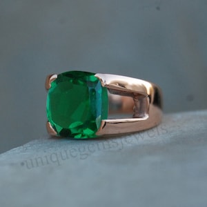 May include: A rose gold ring with a large, emerald green gemstone. The ring has a unique design with a cutout in the band.
