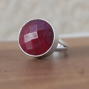 May include: A silver ring with a large, round, faceted ruby gemstone.