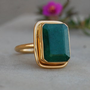 Puede incluir: Un anillo de oro con una gran piedra preciosa verde esmeralda engastada en una forma cuadrada.