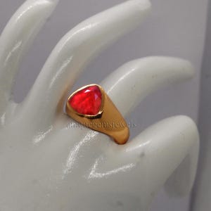 May include: A gold ring with a red gemstone set in a triangular shape. The ring is on a white surface.