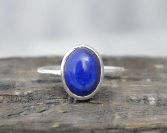 Può includere: Un anello d'argento con una pietra preziosa ovale blu incastonata in una montatura a castone.