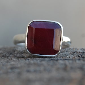 May include: A silver ring with a dark red square gemstone.