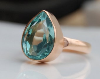 May include: A teardrop-shaped ring with a light blue gemstone set in a rose gold band.