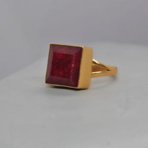 Op de afbeelding: Een gouden ring met een grote, vierkante, rode edelsteen.