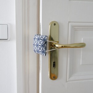 May include: A white door with a gold door handle and a blue and white patterned fabric doorstop.