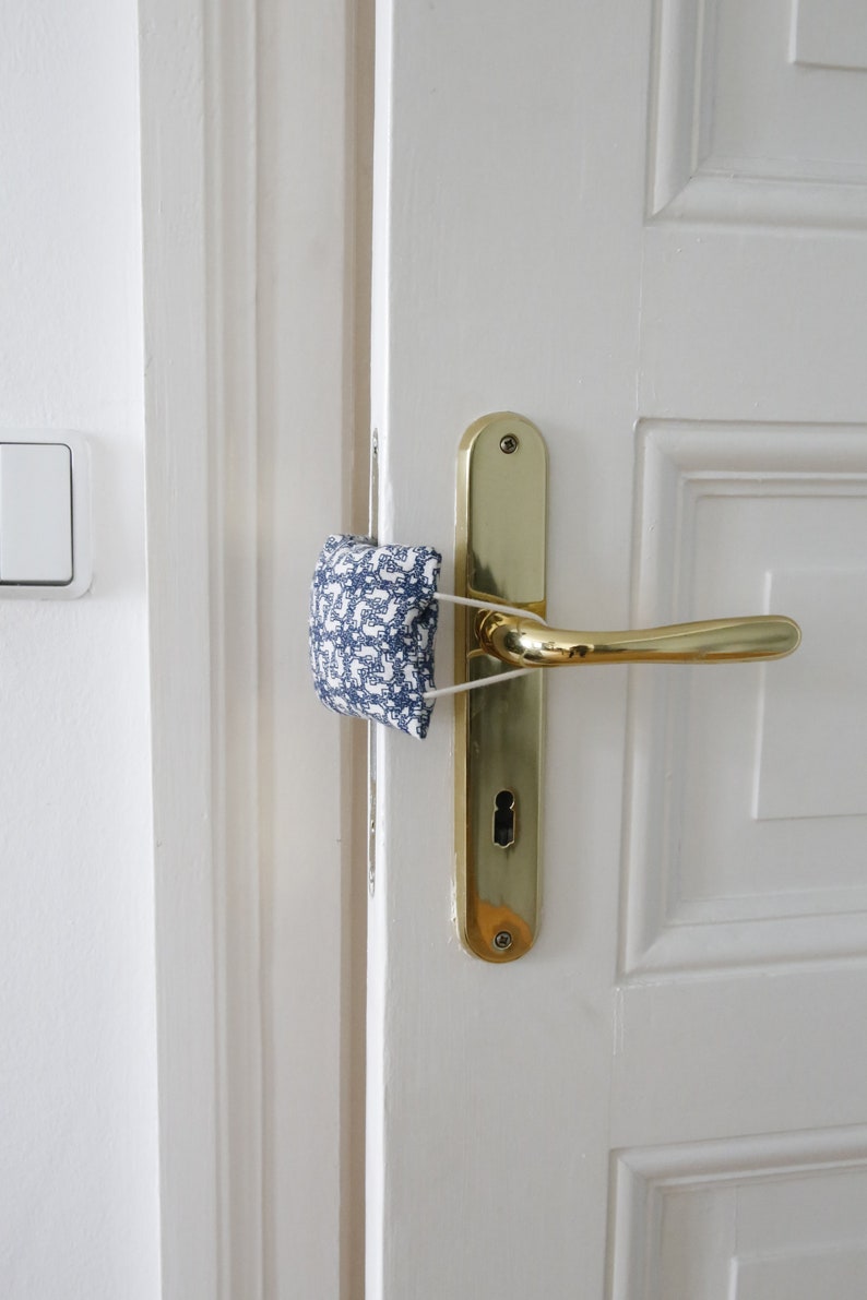 May include: A white door with a gold door handle and a blue and white patterned fabric doorstop.