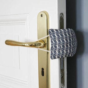 May include: A white door with a gold door handle and a blue and white patterned fabric doorstop attached to the handle with a white elastic band.