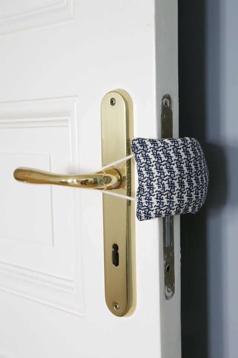 May include: A white door with a gold door handle and a blue and white patterned fabric doorstop attached to the handle with a white elastic band.