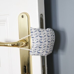 May include: A white door with a gold door handle and a blue and white patterned fabric doorstop.