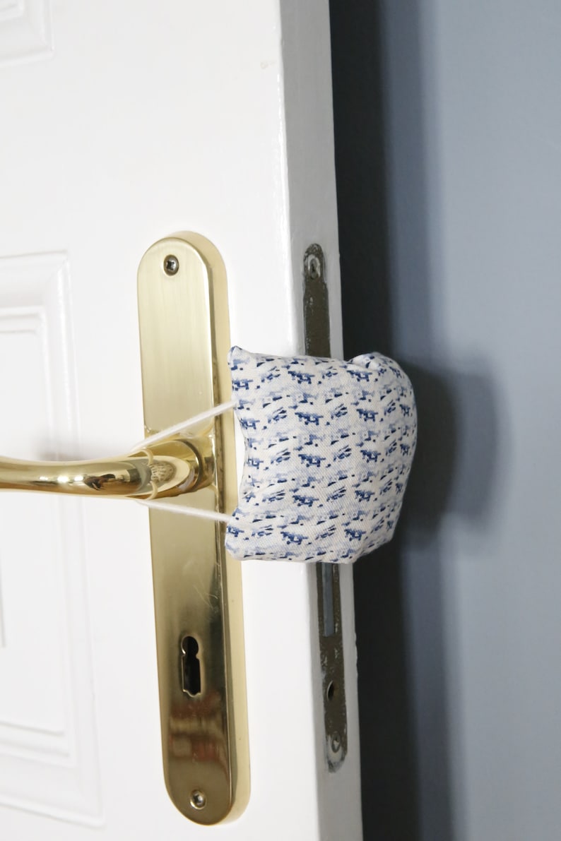 May include: A white door with a gold door handle and a blue and white patterned fabric doorstop.
