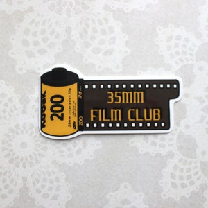 May include: A black and yellow sticker with a film canister and film strip design. The sticker says "35mm Film Club" and "200" on the canister.