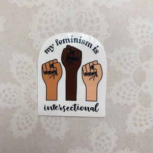 May include: A white sticker with an arched design featuring three raised fists in different skin tones. The text "my feminism is intersectional" is written in black below the fists.