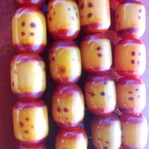 Puede incluir: Una cadena de cuentas amarillas y rojas con manchas negras. Las cuentas son redondas y tienen un acabado brillante.