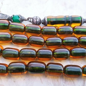 Puede incluir: Unas cuentas de oración de ámbar rayadas en marrón y verde con un borla de plata y verde.